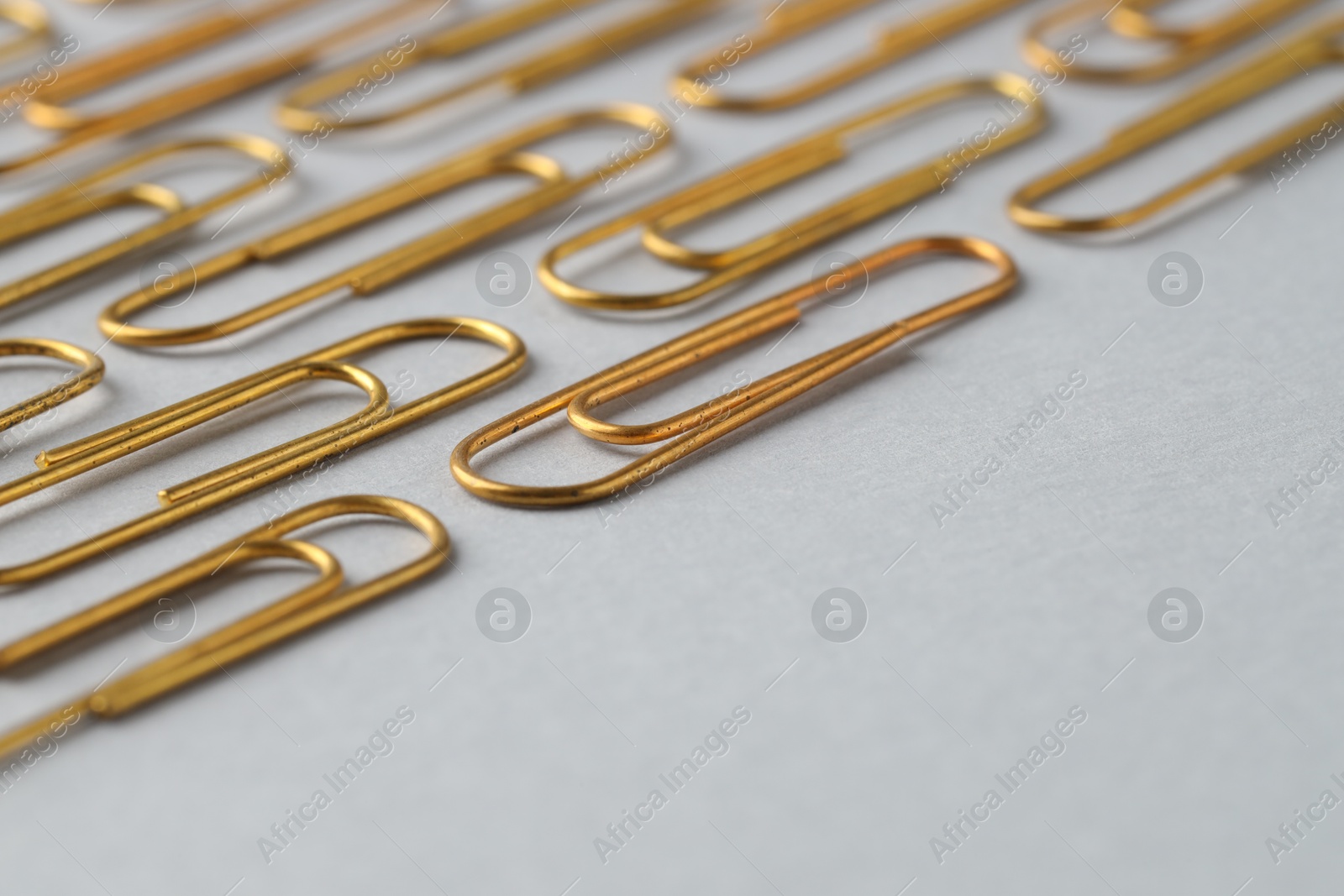 Photo of Golden paper clips on light background, closeup