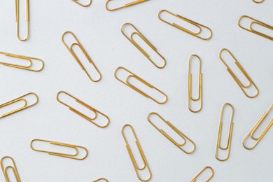 Photo of Golden paper clips on light background, flat lay