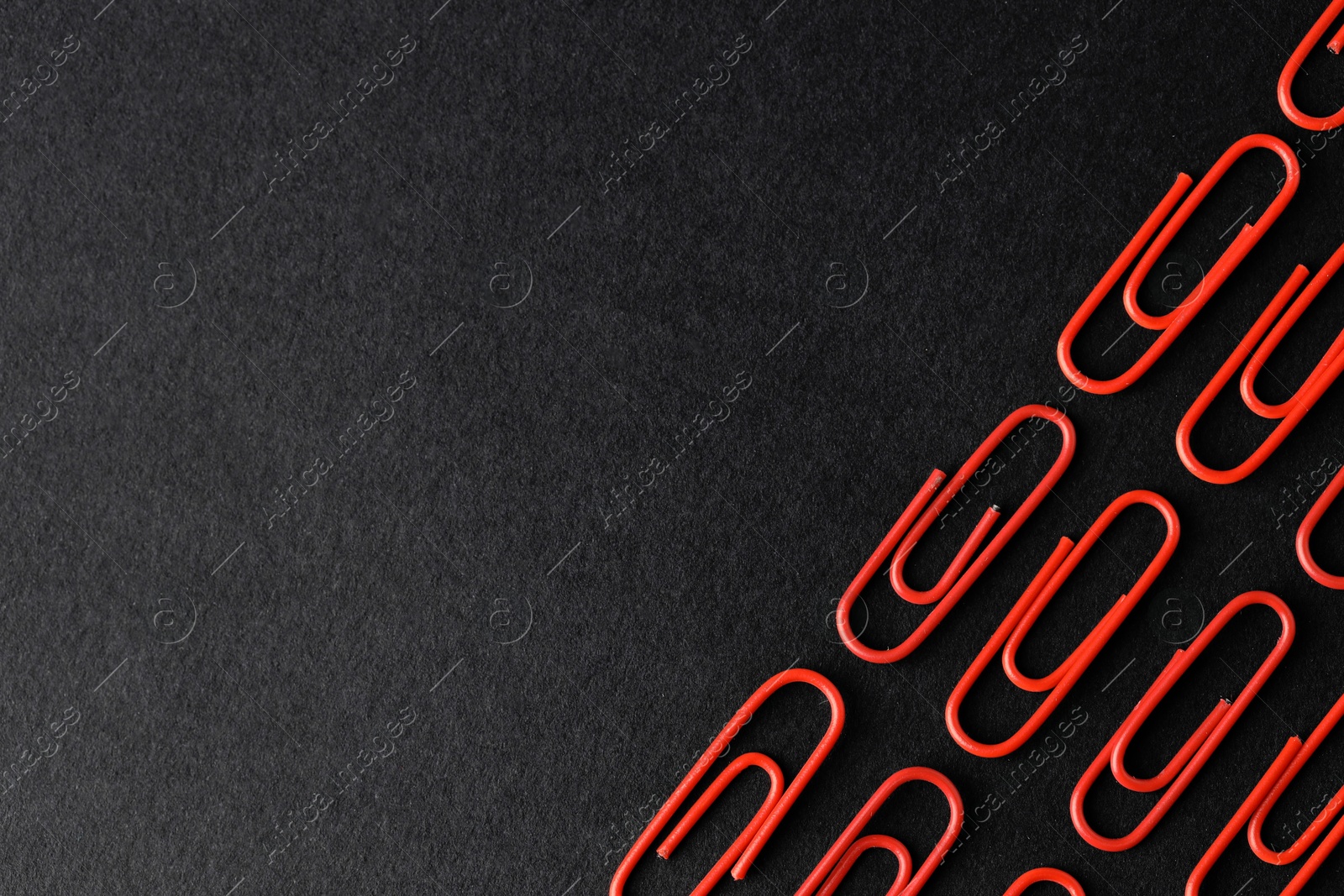 Photo of Red paper clips on black background, flat lay. Space for text