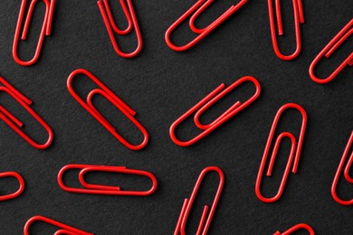 Photo of Red paper clips on black background, flat lay