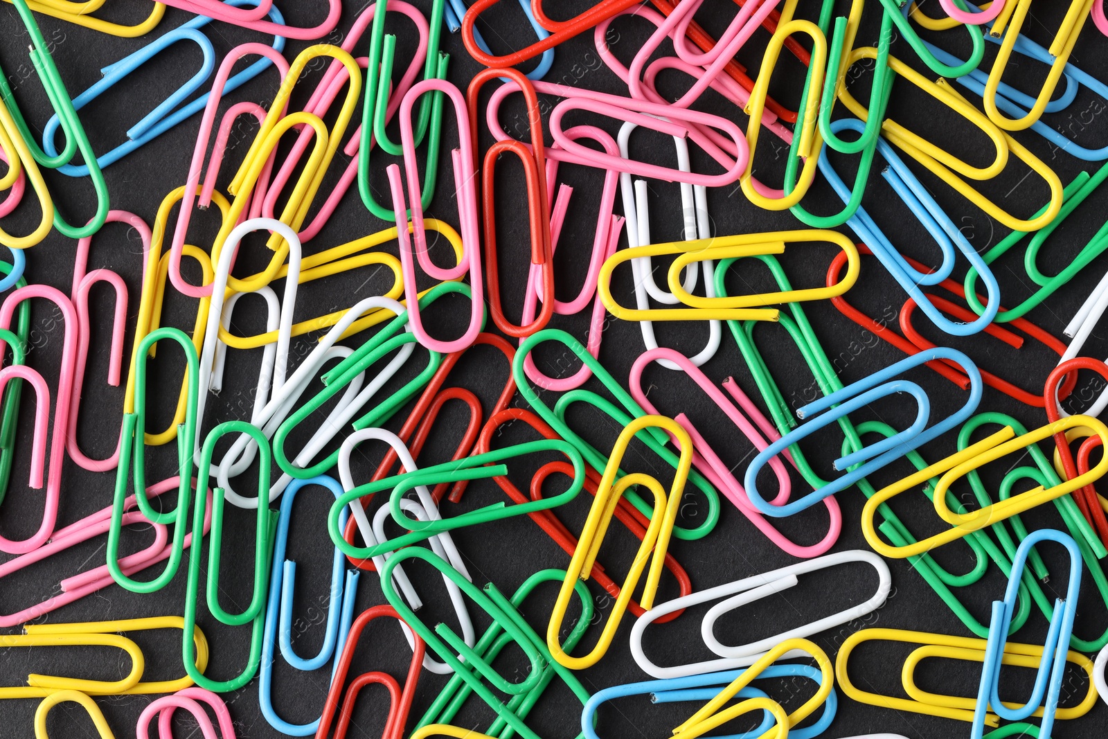 Photo of Colorful paper clips on black background, flat lay