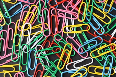 Photo of Colorful paper clips on black background, flat lay