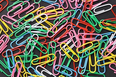 Photo of Colorful paper clips on black background, flat lay