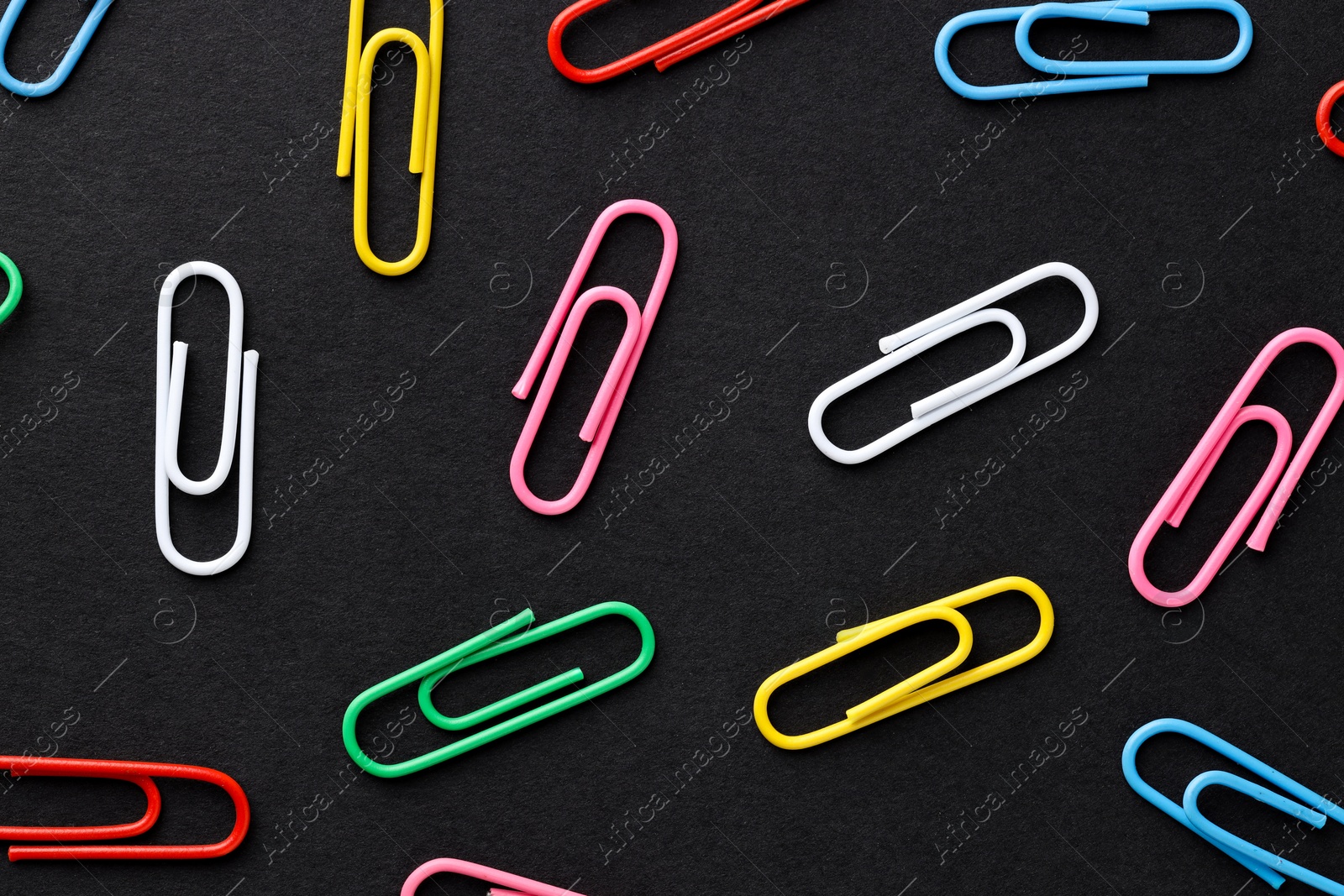 Photo of Colorful paper clips on black background, flat lay