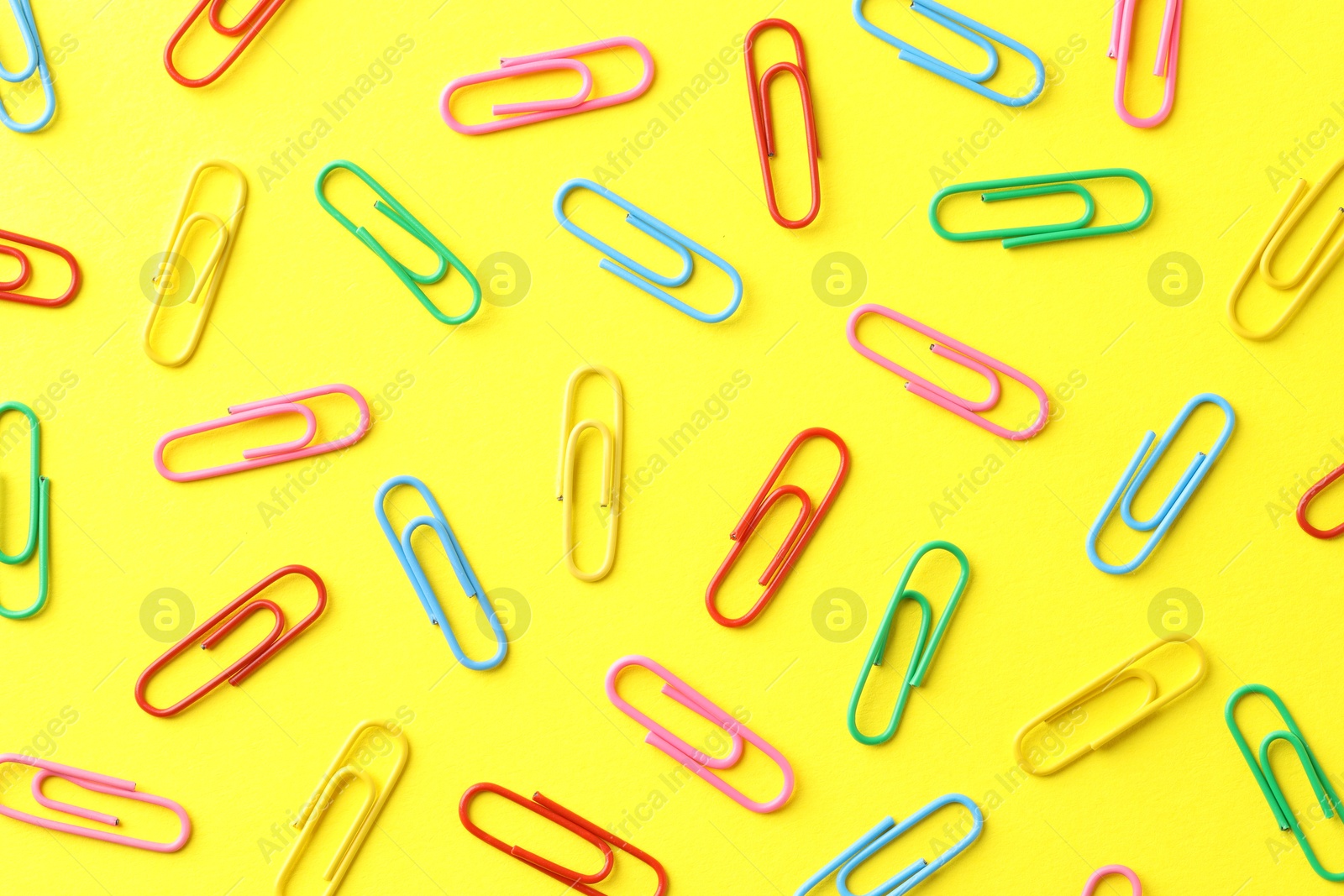 Photo of Colorful paper clips on yellow background, flat lay