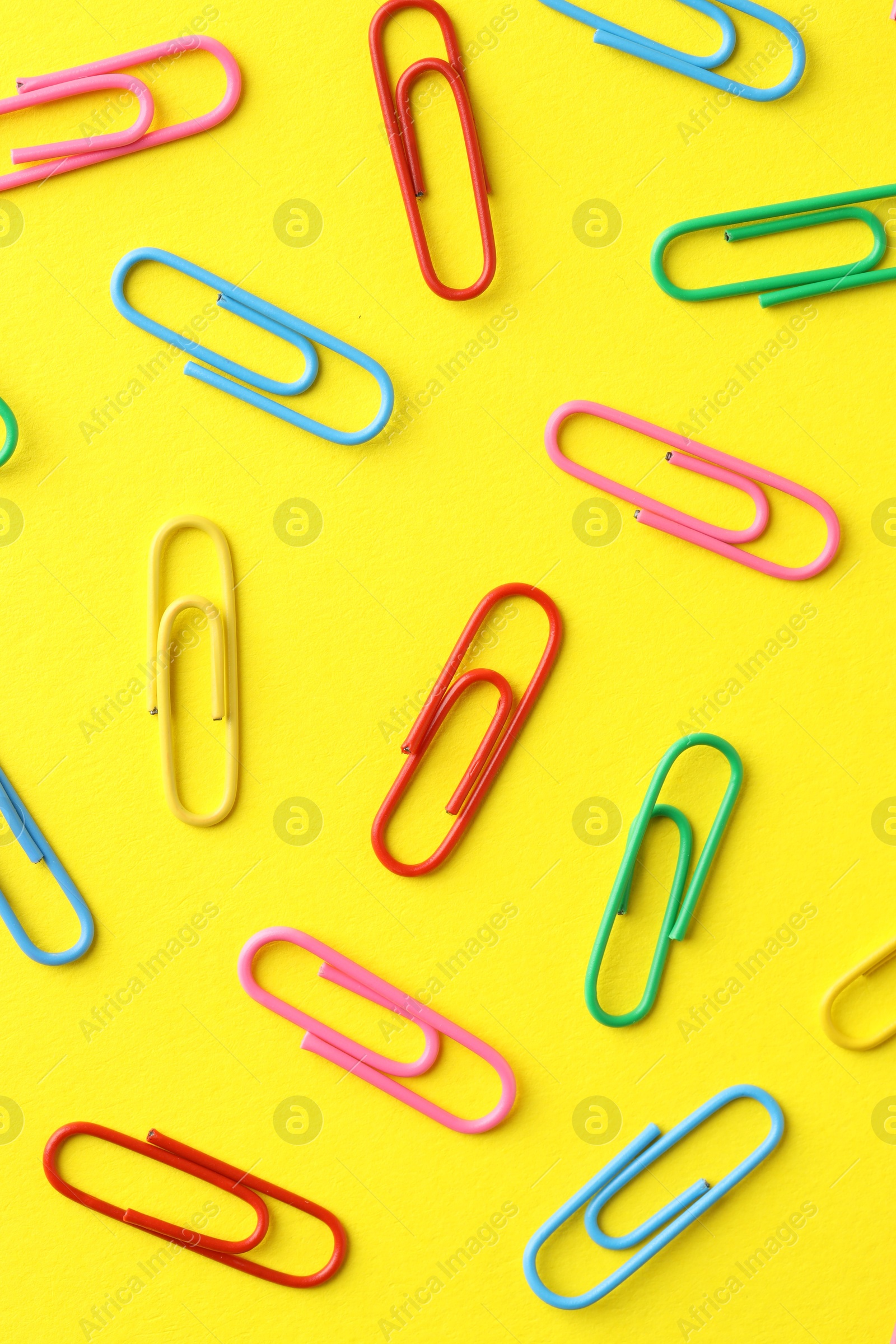 Photo of Colorful paper clips on yellow background, flat lay