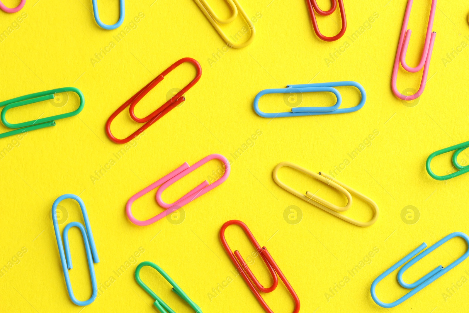 Photo of Colorful paper clips on yellow background, flat lay