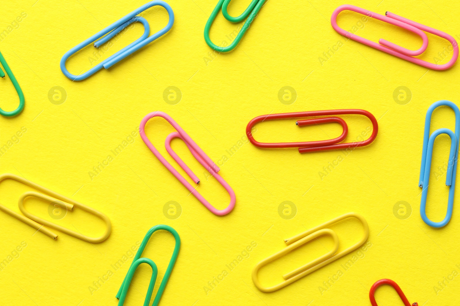 Photo of Colorful paper clips on yellow background, flat lay