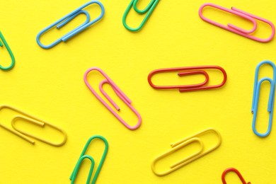 Photo of Colorful paper clips on yellow background, flat lay