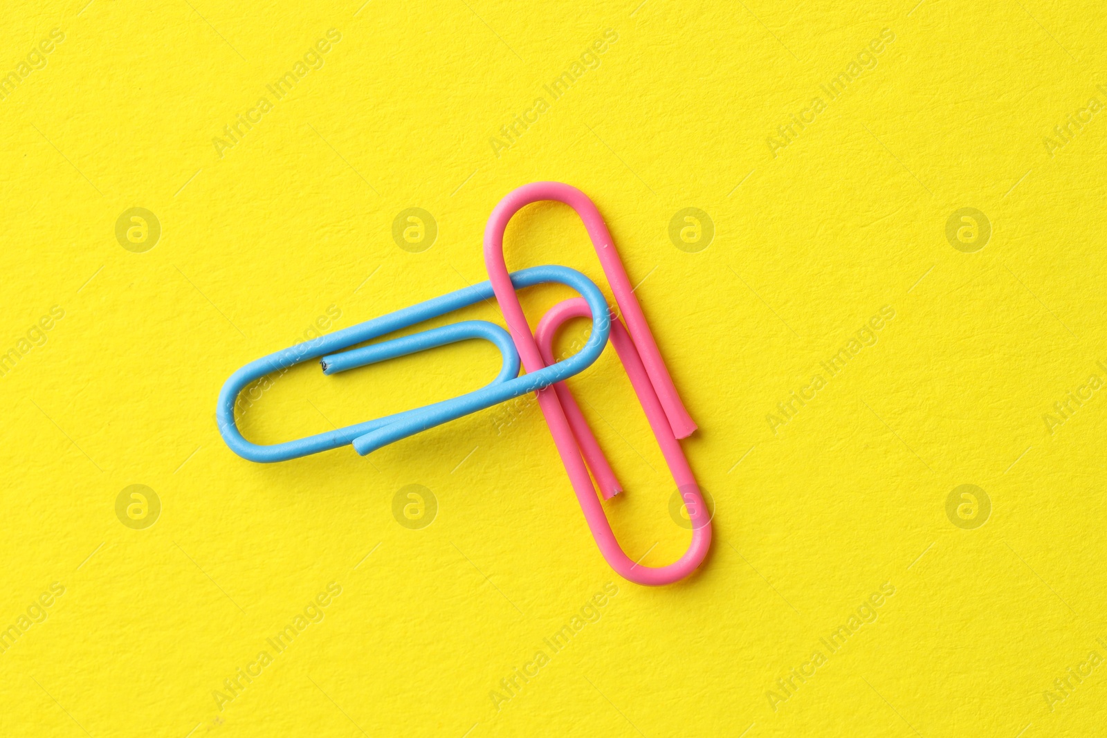 Photo of Two paper clips on yellow background, top view