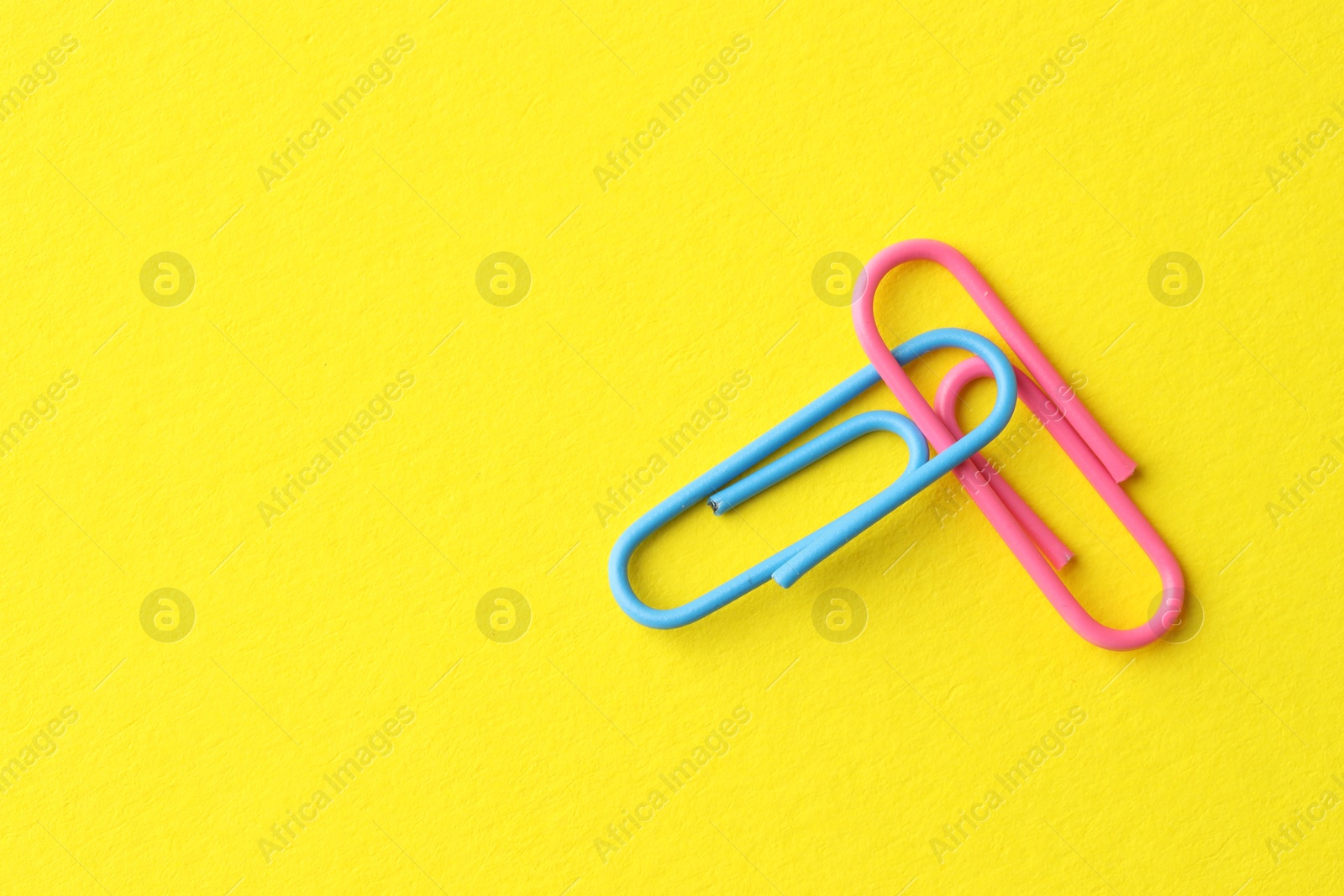 Photo of Two paper clips on yellow background, top view. Space for text