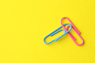 Photo of Two paper clips on yellow background, top view. Space for text