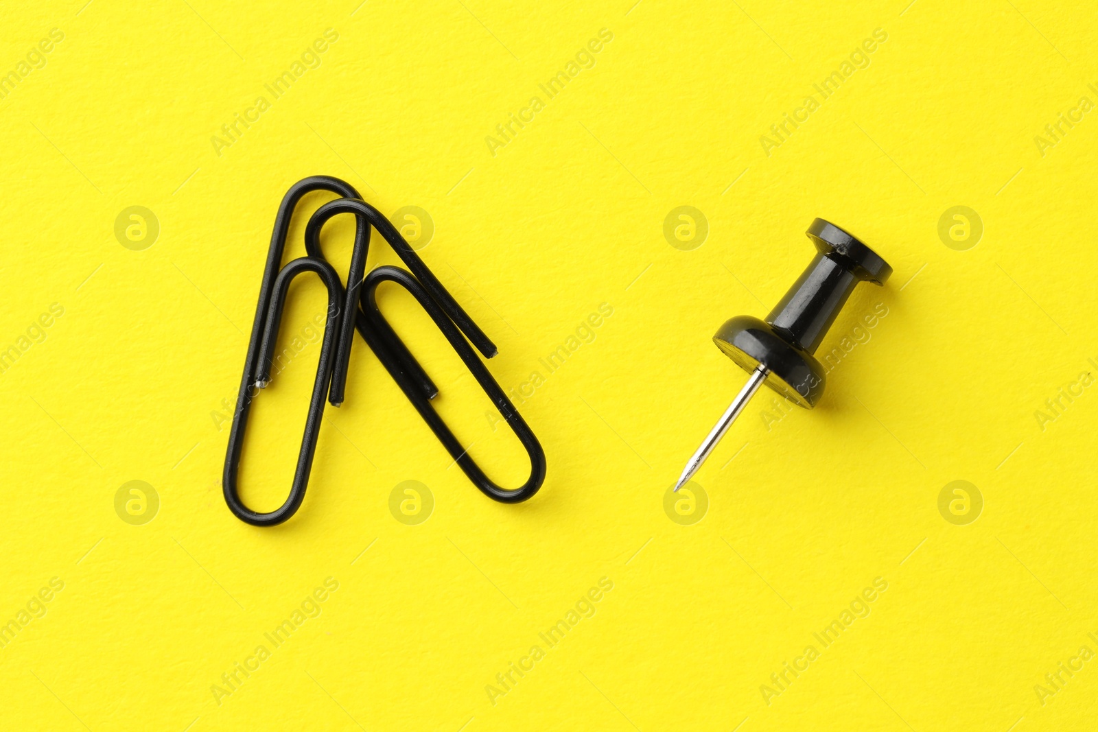 Photo of Paper clips and pin on yellow background, top view