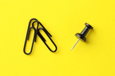 Paper clips and pin on yellow background, top view