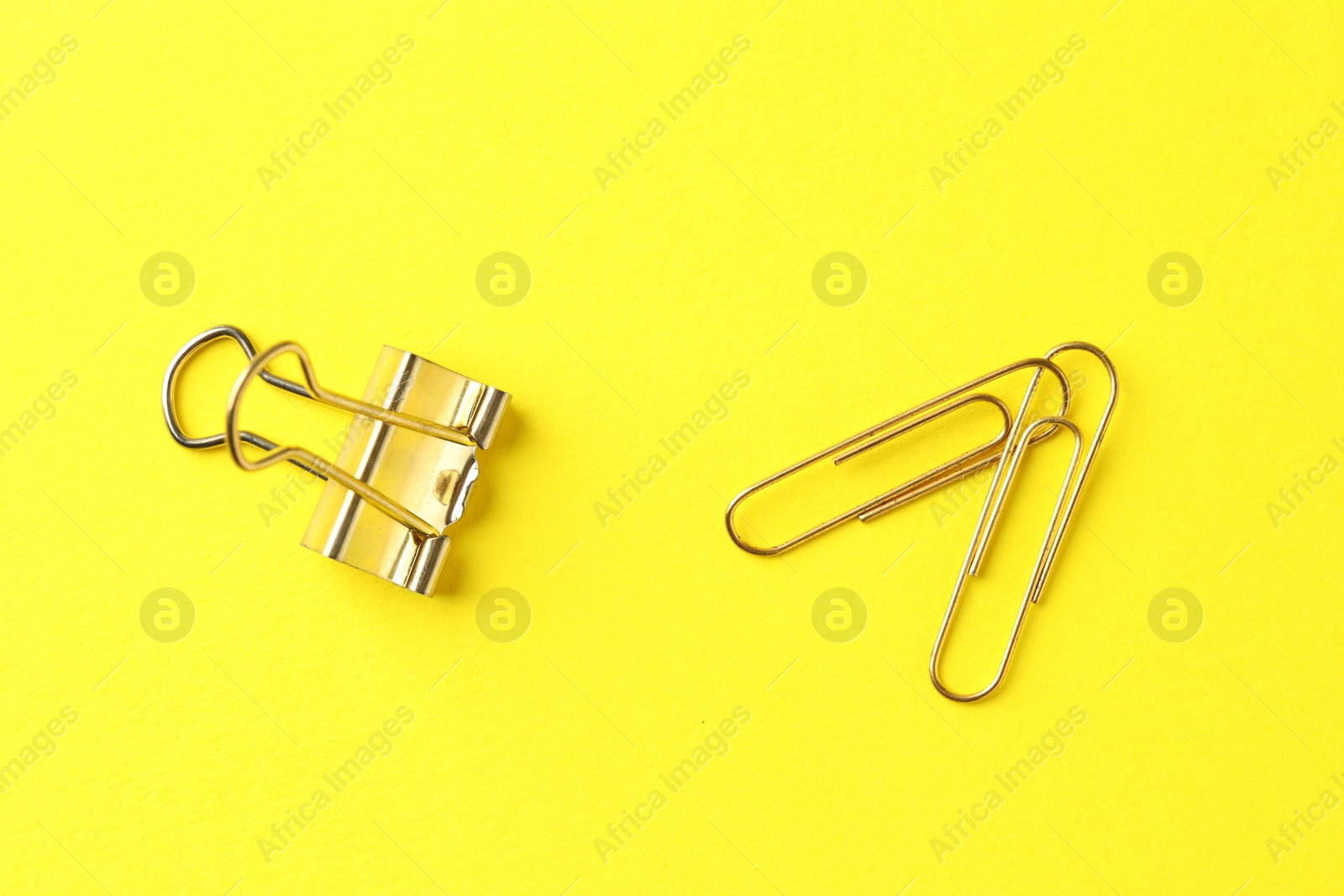 Photo of Golden paper clips on yellow background, flat lay