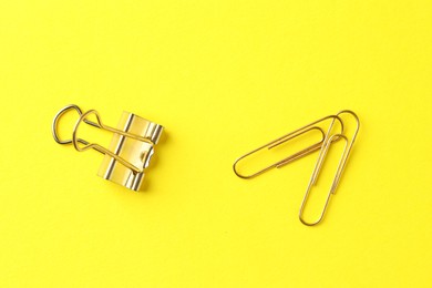 Photo of Golden paper clips on yellow background, flat lay