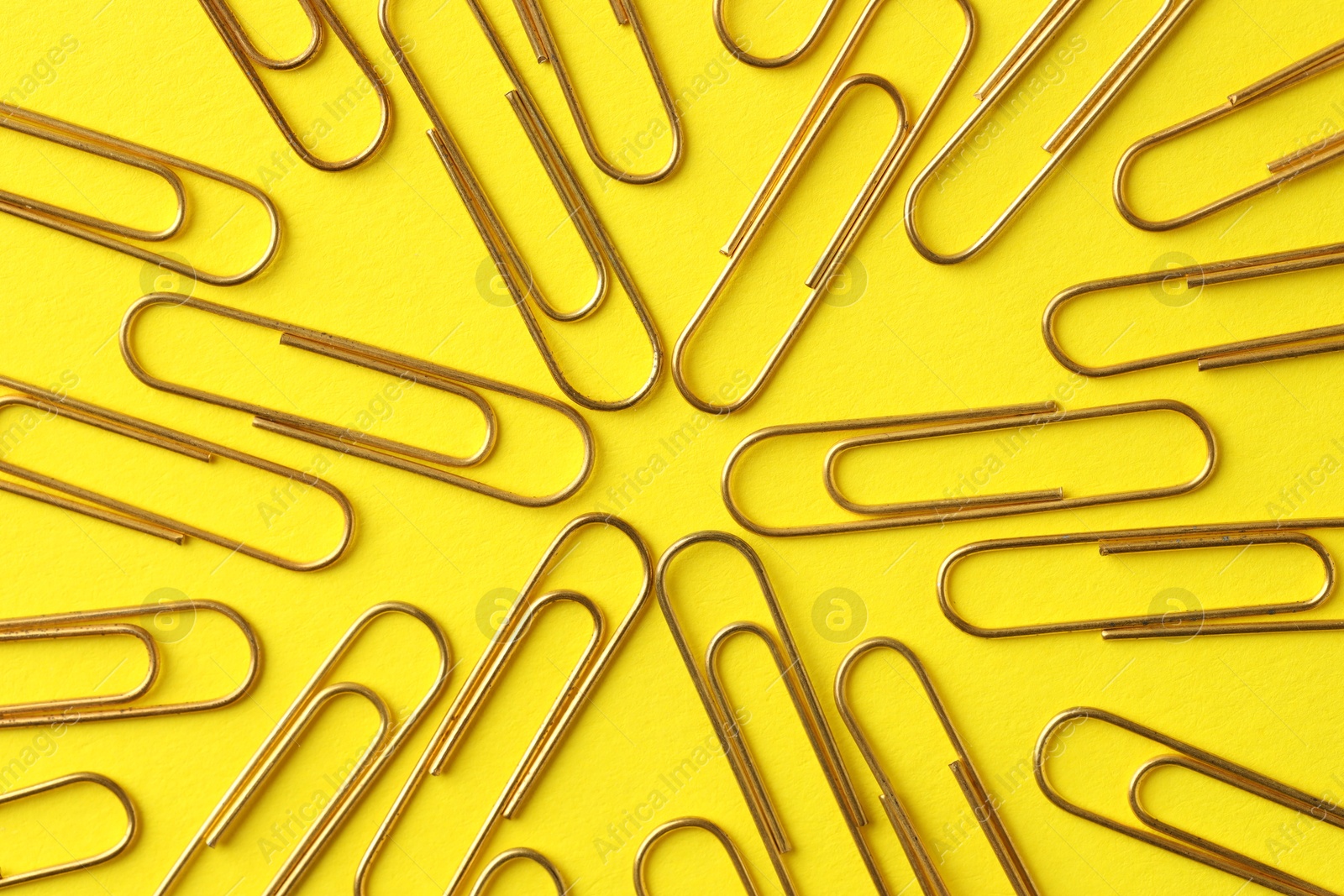 Photo of Golden paper clips on yellow background, flat lay