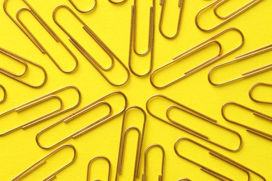 Photo of Golden paper clips on yellow background, flat lay