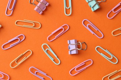 Photo of Colorful paper clips on orange background, flat lay