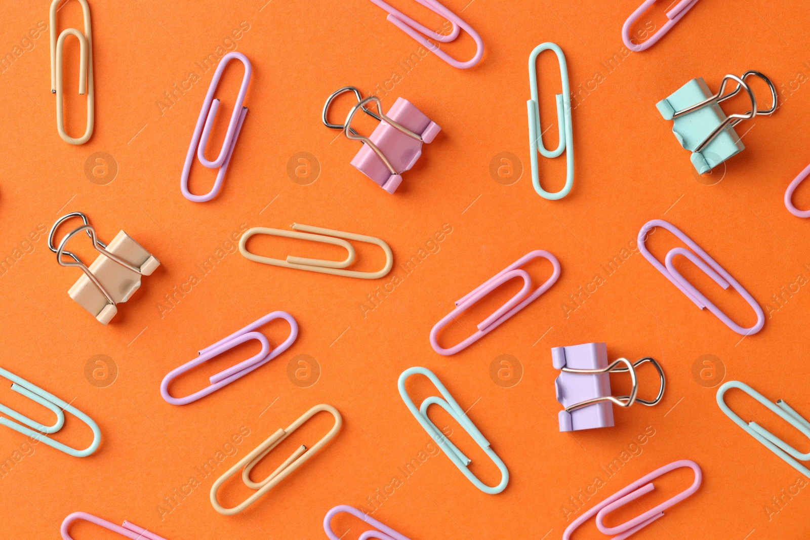 Photo of Colorful paper clips on orange background, flat lay