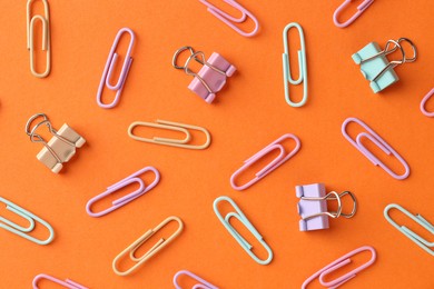 Photo of Colorful paper clips on orange background, flat lay