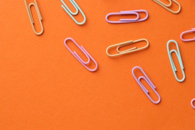 Photo of Colorful paper clips on orange background, flat lay. Space for text