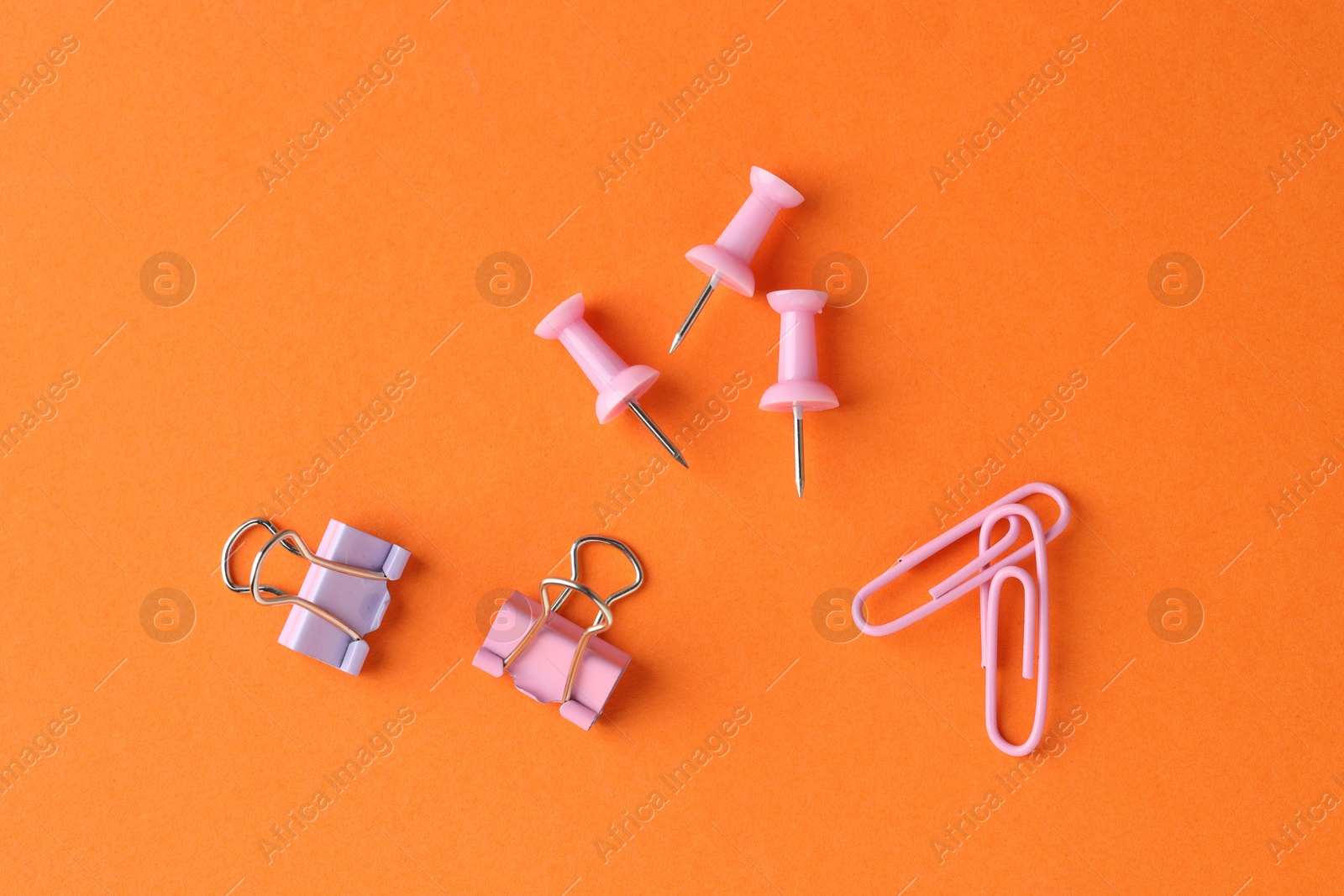 Photo of Paper clips and pins on orange background, flat lay