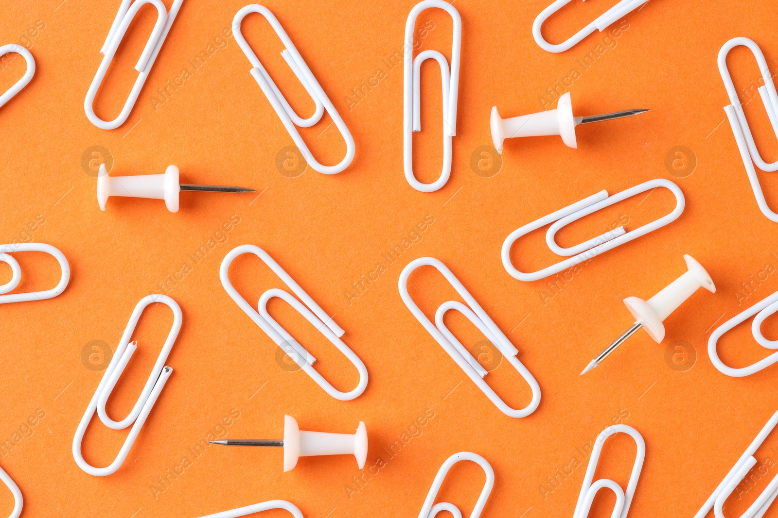 Photo of Paper clips and pins on orange background, flat lay