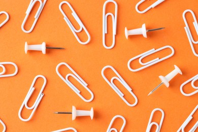 Paper clips and pins on orange background, flat lay