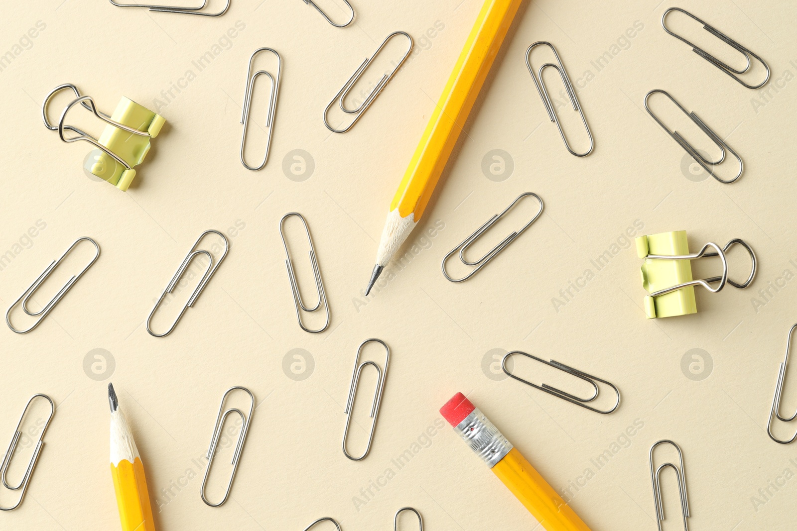 Photo of Paper clips and pencils on beige background, flat lay