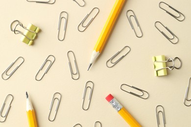 Photo of Paper clips and pencils on beige background, flat lay