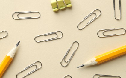 Photo of Paper clips and pencils on beige background, flat lay