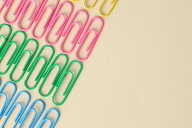 Colorful paper clips on beige background, flat lay. Space for text