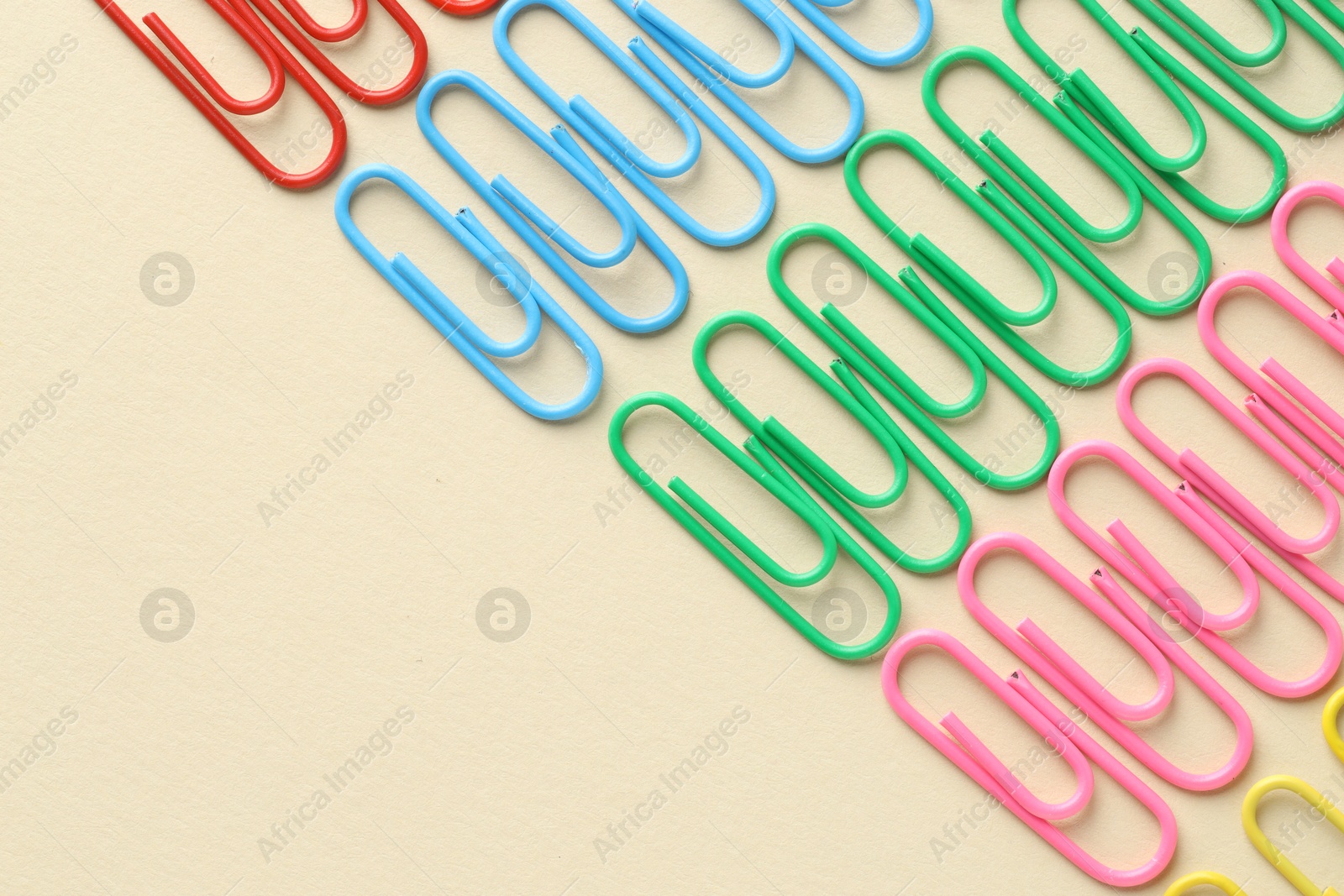 Photo of Colorful paper clips on beige background, flat lay. Space for text