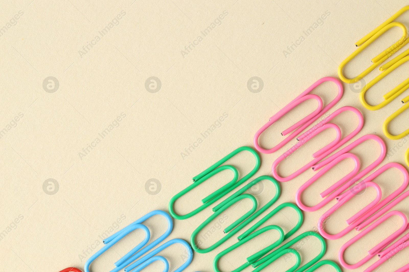 Photo of Colorful paper clips on beige background, flat lay. Space for text