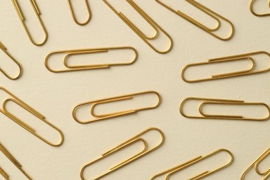 Golden paper clips on beige background, flat lay