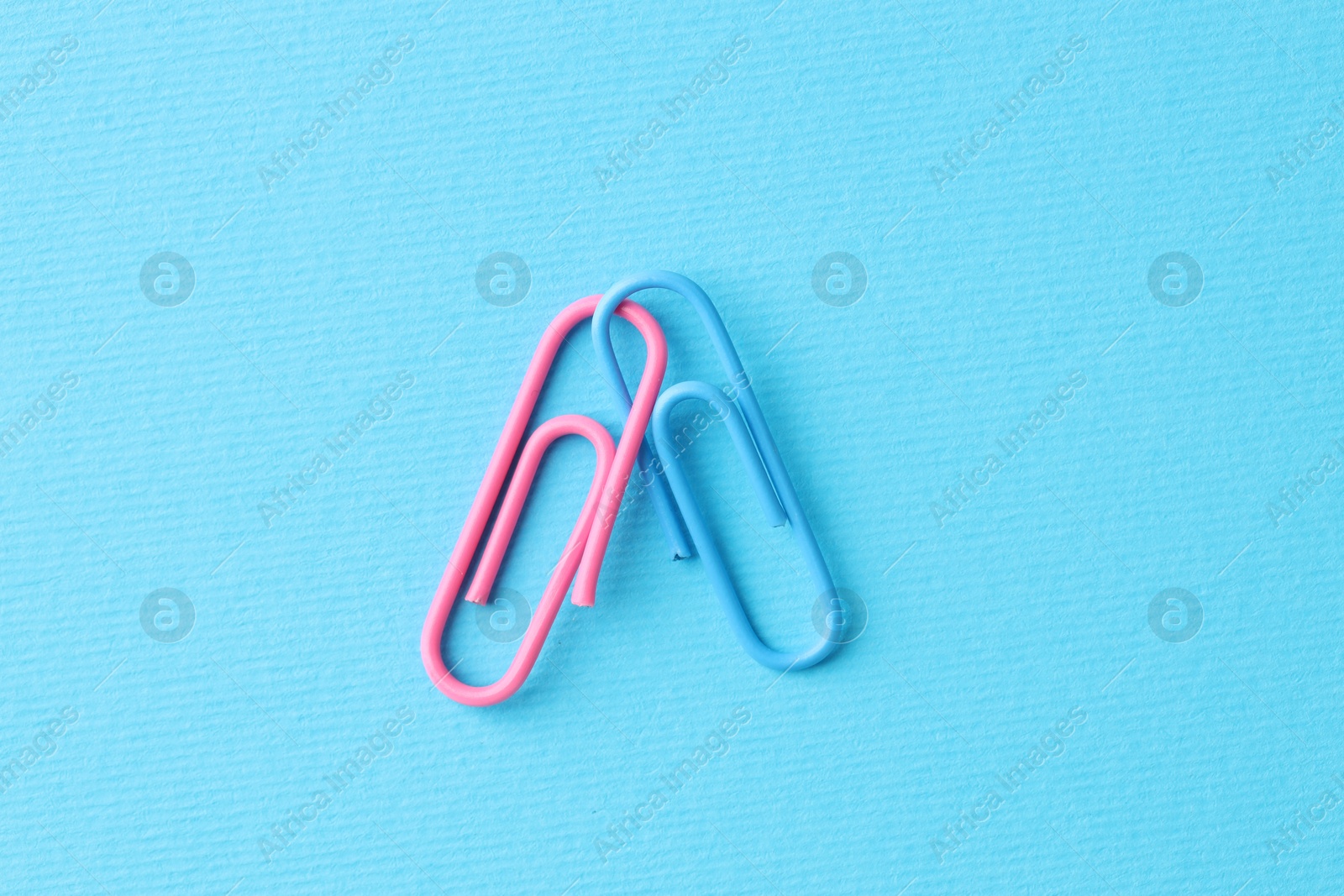 Photo of Two paper clips on light blue background, top view