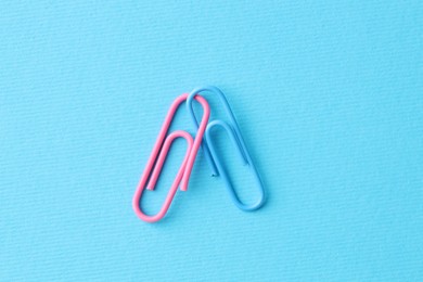 Photo of Two paper clips on light blue background, top view