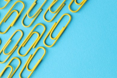 Photo of Many paper clips on light blue background, flat lay. Space for text