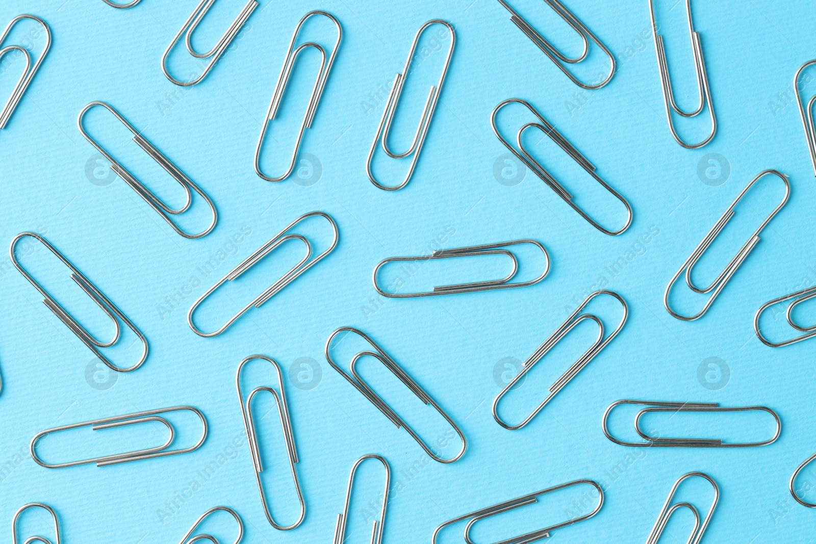 Photo of Metal paper clips on light blue background, flat lay