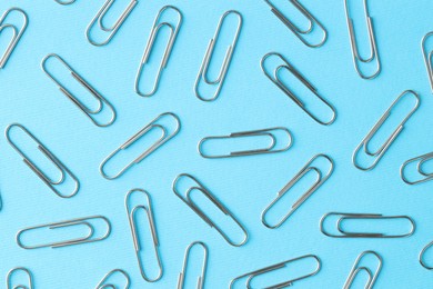 Metal paper clips on light blue background, flat lay