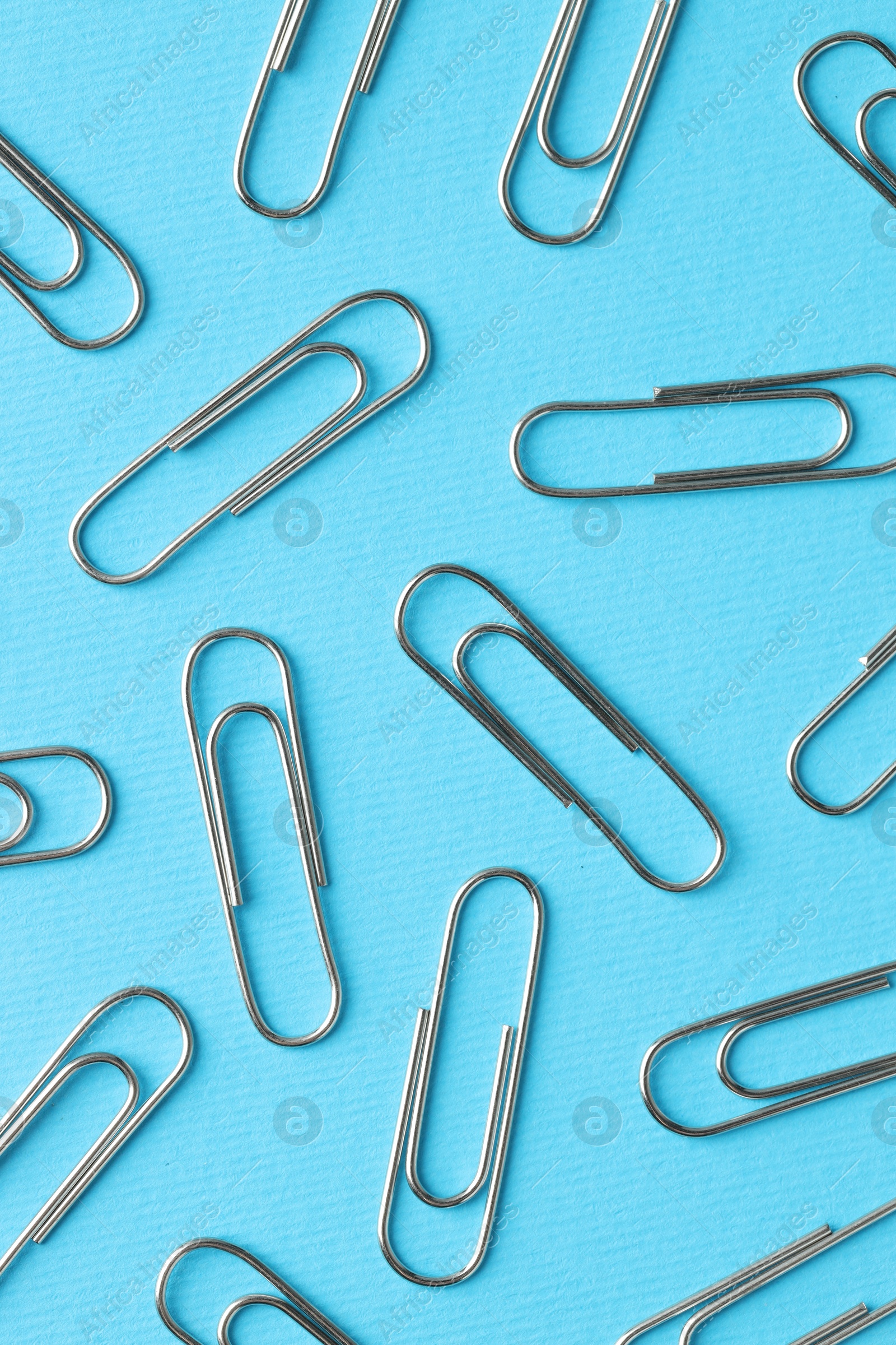 Photo of Metal paper clips on light blue background, flat lay