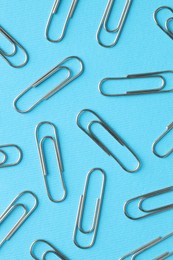 Metal paper clips on light blue background, flat lay