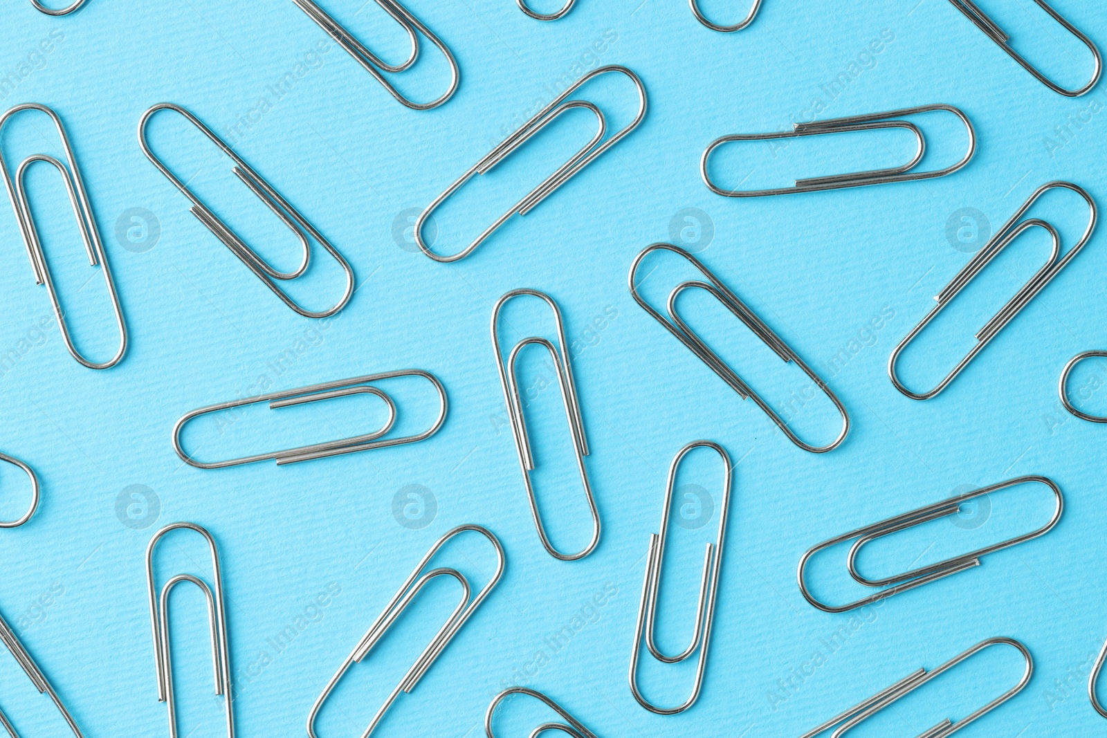 Photo of Metal paper clips on light blue background, flat lay