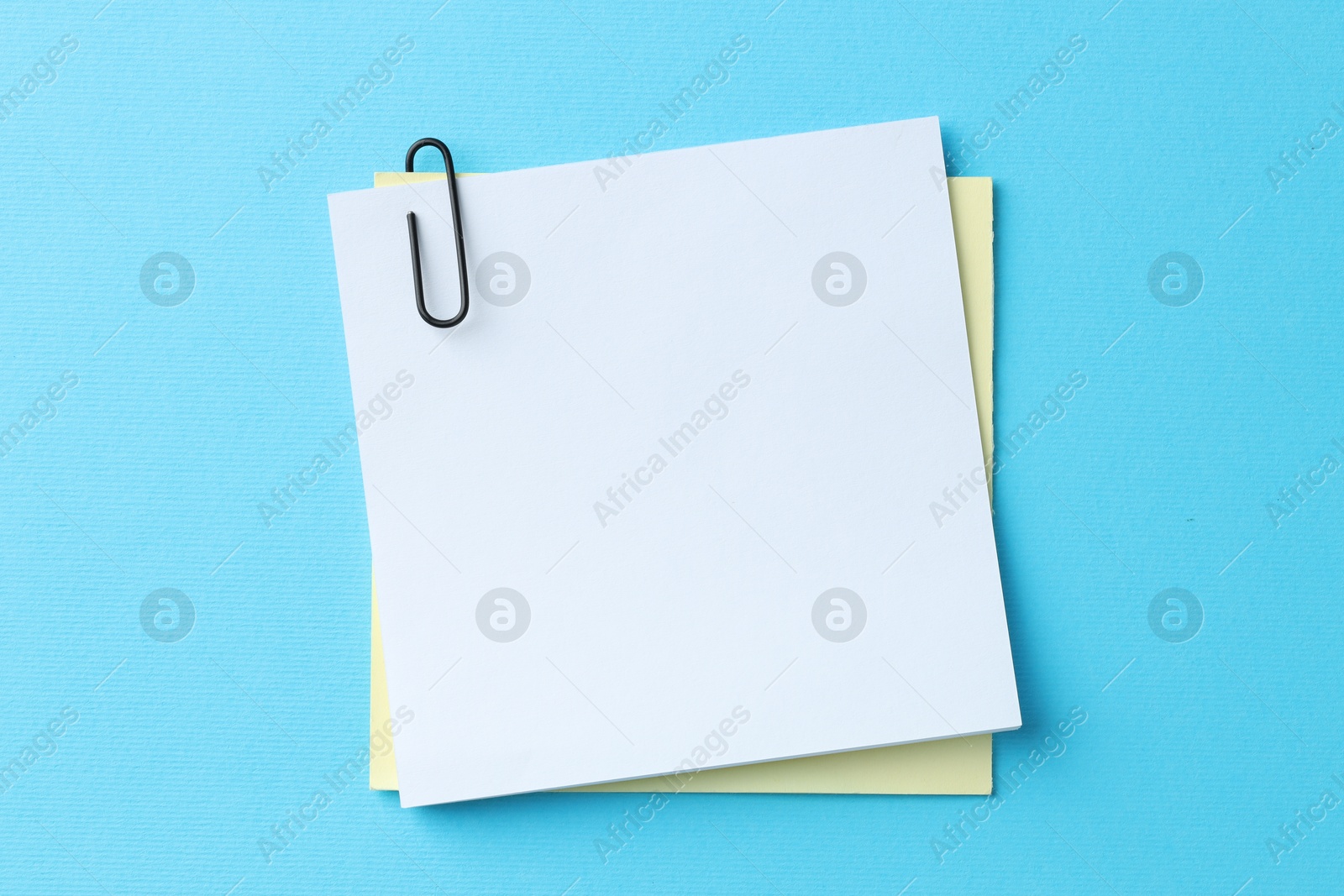 Photo of Paper notes with clip on light blue background, top view. Space for text