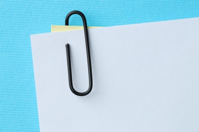 Photo of Paper notes with clip on light blue background, top view. Space for text