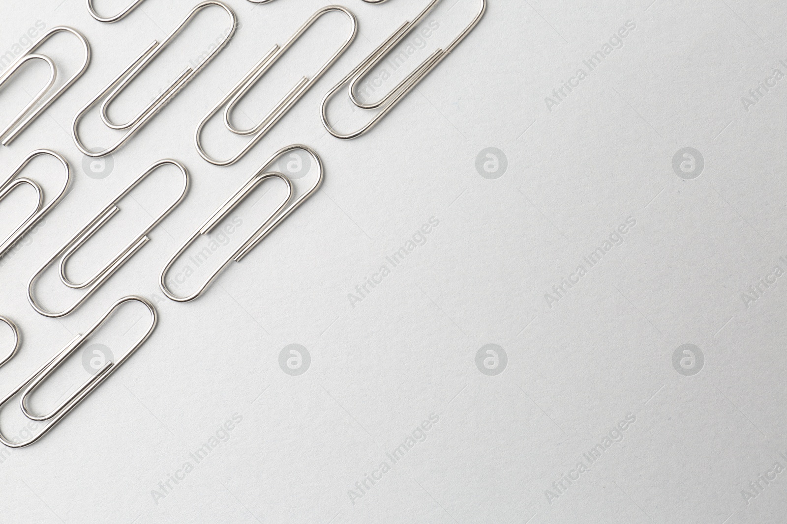 Photo of Metal paper clips on light background, flat lay. Space for text