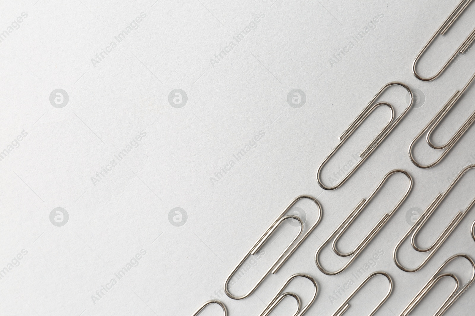 Photo of Metal paper clips on light background, flat lay. Space for text