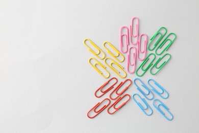 Photo of Colorful paper clips on light background, flat lay. Space for text