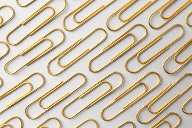 Photo of Golden paper clips on light background, flat lay